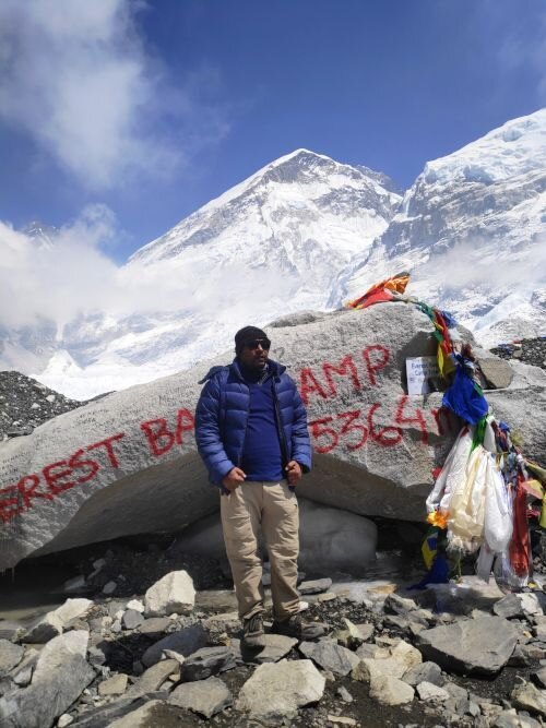Navaraj Thapa at the Everest Base Camp marker rock, 5,364 m, with prayer flags and the peak behind