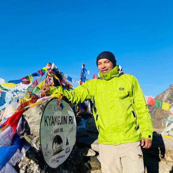 Navaraj Thapa beside the Lower Kyangjin Ri sign at 4,400 m in Langtang, among prayer flags